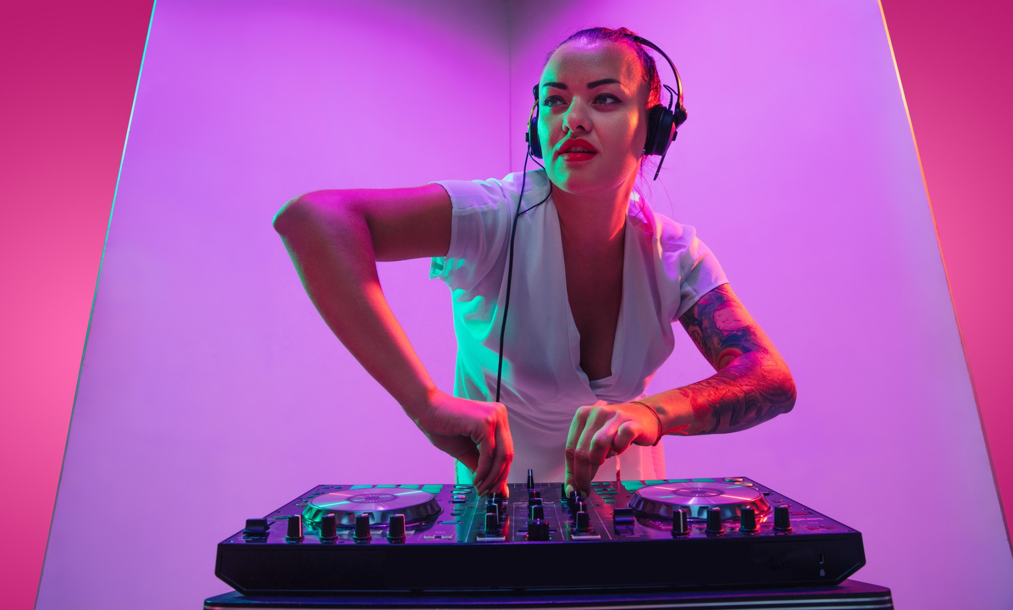 Summertime. Young female musician in headphones performing on purple background in neon light. Concept of music, hobby, festival, entertainment, emotions. Joyful party host, DJ, portrait of artist.